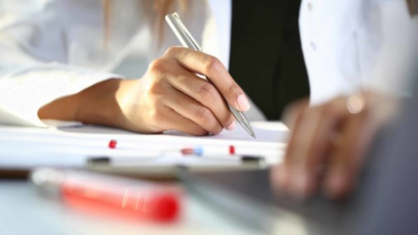 Female medicine doctor hand hold siver pen and write prescription to patient at worktable. Panacea and life save, prescribing treatment, legal drug store concept. Empty form ready to be used